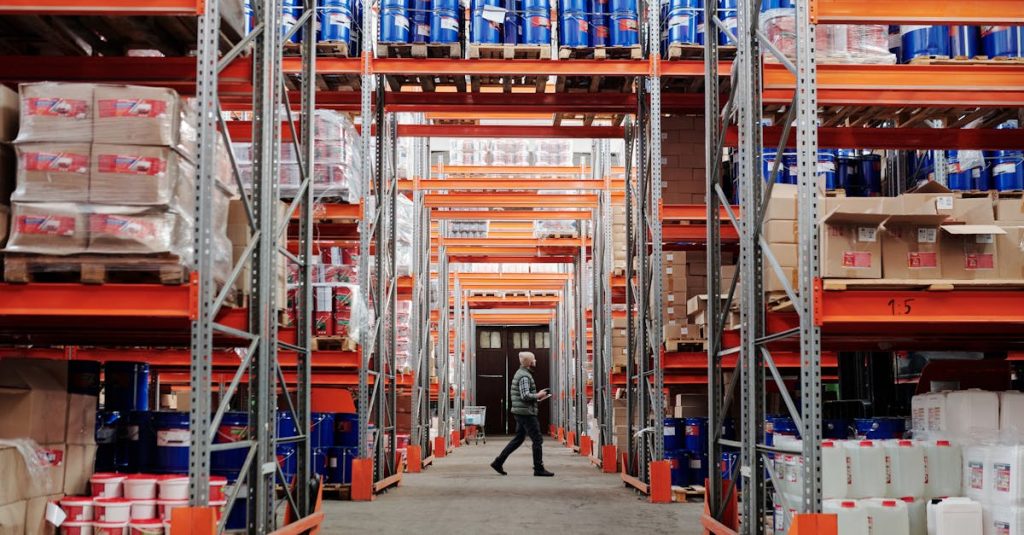 Warehouse management - A man walking through a large industrial warehouse with stacked shelves filled with goods and products.